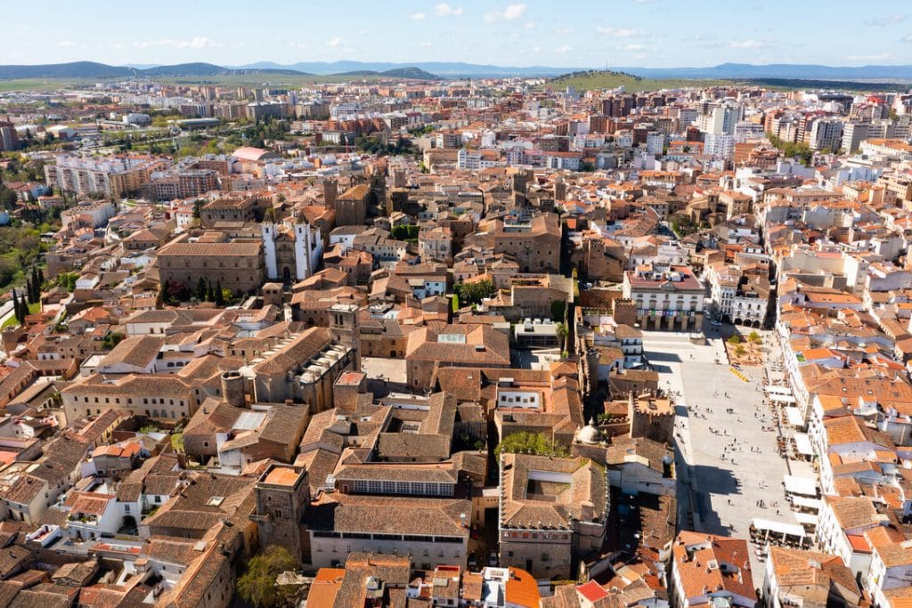 Aerial view of a densely built town with terracotta roofs and a large square plaza filled with people, surrounded by historic buildings.&nbsp;Hispamer Noticias