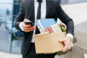 Businessperson in a suit carries a cardboard box with personal items and checks a smartphone&nbsp;Hispamer Noticias