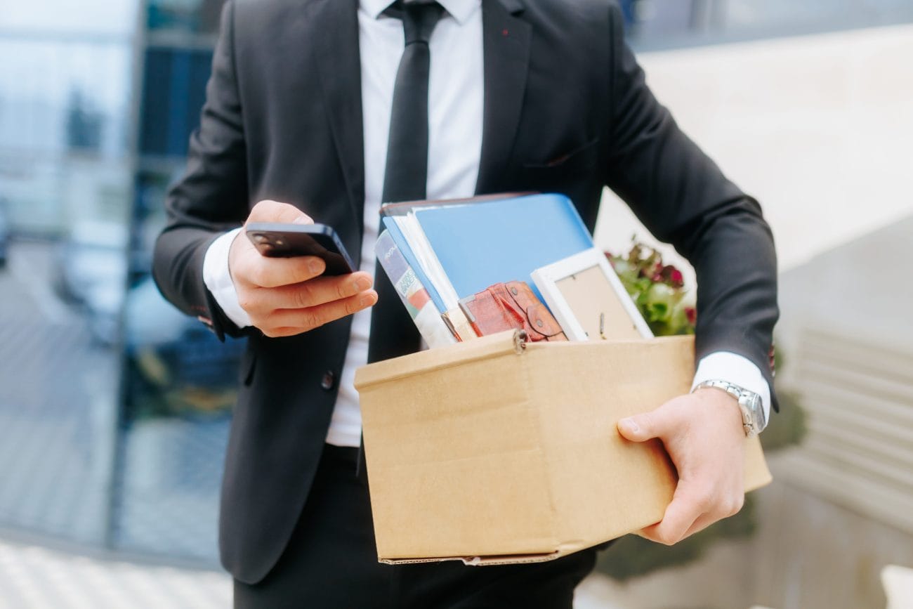 Businessperson in a suit carries a cardboard box with personal items and checks a smartphone&nbsp;Hispamer Noticias
