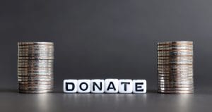 Stacks of coins flank the word DONATE formed by letter blocks, signaling fundraising or contribution appeal.&nbsp;Hispamer Noticias