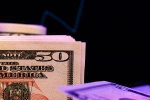Stack of US $50 bills fanned in the foreground under purple lighting with a dark background&nbsp;Hispamer Noticias