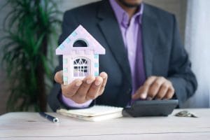 763812 - González Martínez - Hispamer Noticias Businessperson in a suit presenting a pastel toy house over a desk with a calculator. Hispamer Noticias