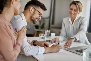Man signs documents at a conference table while two colleagues look on and smile.&nbsp;Hispamer Noticias