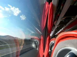 Bus interior with red curtains and grey seats; outside a highway, hills, and blue sky visible through the window.&nbsp;Hispamer Noticias