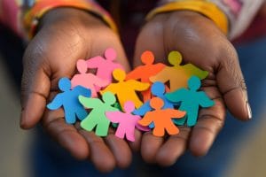 Two hands cup a handful of multicolored paper people shapes, symbolizing community and diversity.&nbsp;Hispamer Noticias