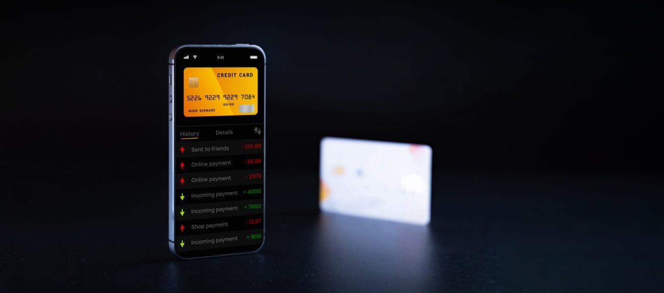 Smartphone screen showing a yellow credit card in a finance app with a transaction list; a blurred card sits in the background on a dark surface.&nbsp;Hispamer Noticias