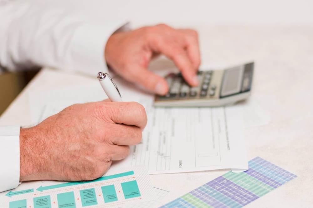 773652 - Carbonell Consultors Associats - Hispamer Noticias Person filling out financial forms with a pen while using a calculator on a desk, with color charts nearby. Hispamer Noticias