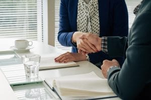 773732 - Briones Abogados - Hispamer Noticias Two professionals shake hands over a desk with notebooks, signaling an agreement in a meeting setting Hispamer Noticias