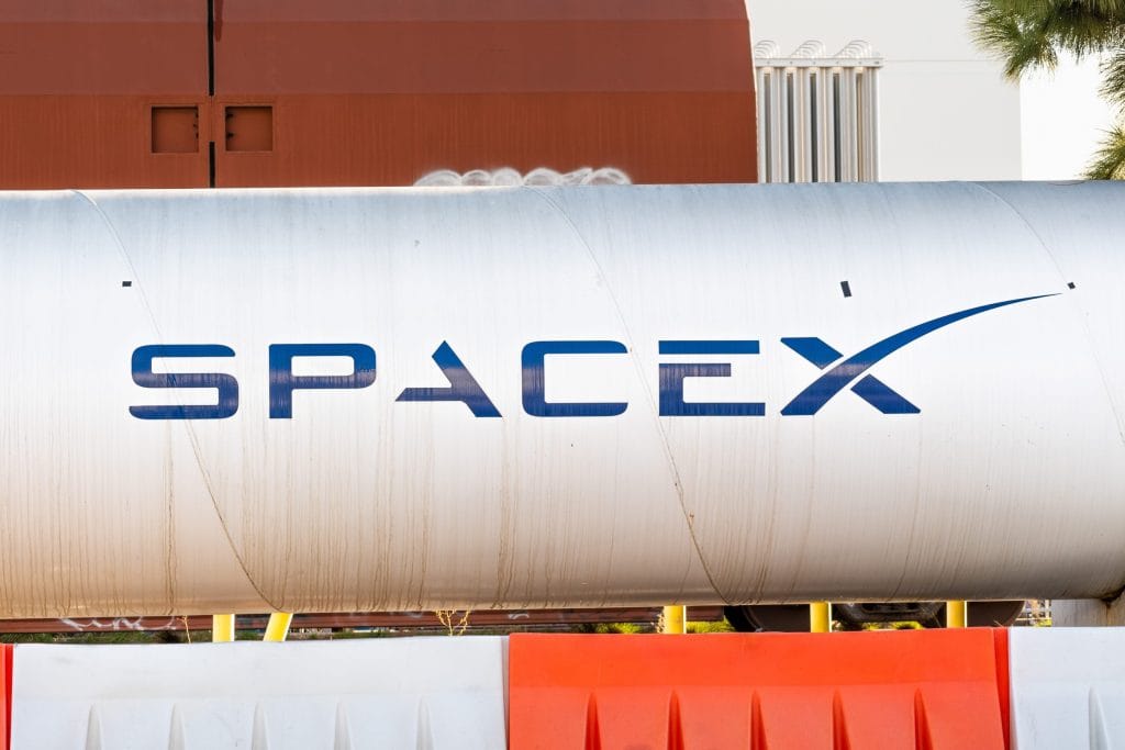 SpaceX logo on a large silver rocket tank with an orange building in the background.&nbsp;Hispamer Noticias