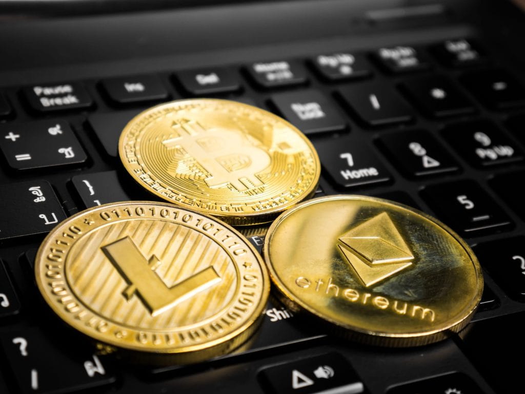 Gold cryptocurrency coins—Bitcoin, Ethereum, and Litecoin—resting on a laptop keyboard.&nbsp;Hispamer Noticias
