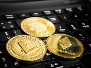 Gold cryptocurrency coins—Bitcoin, Ethereum, and Litecoin—resting on a laptop keyboard.&nbsp;Hispamer Noticias