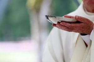 Priest's hands holding a silver communion spoon during a Christian service.&nbsp;Hispamer Noticias