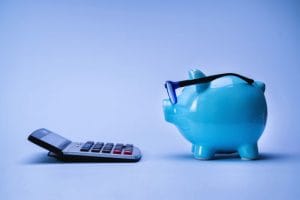 777984 - Consulae - Hispamer Noticias Blue piggy bank wearing glasses sits beside a calculator on a blue background, signaling saving and budgeting. Hispamer Noticias
