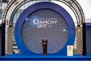 Speaker at a podium on a blue circular stage for an opening ceremony with a large screen reading 'Opening Ceremony' and event name/date in the background&nbsp;Hispamer Noticias