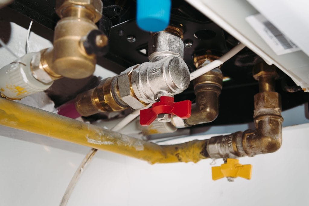 Close-up of exposed plumbing with a red-handled valve and yellow pipe under a device or sink.&nbsp;Hispamer Noticias