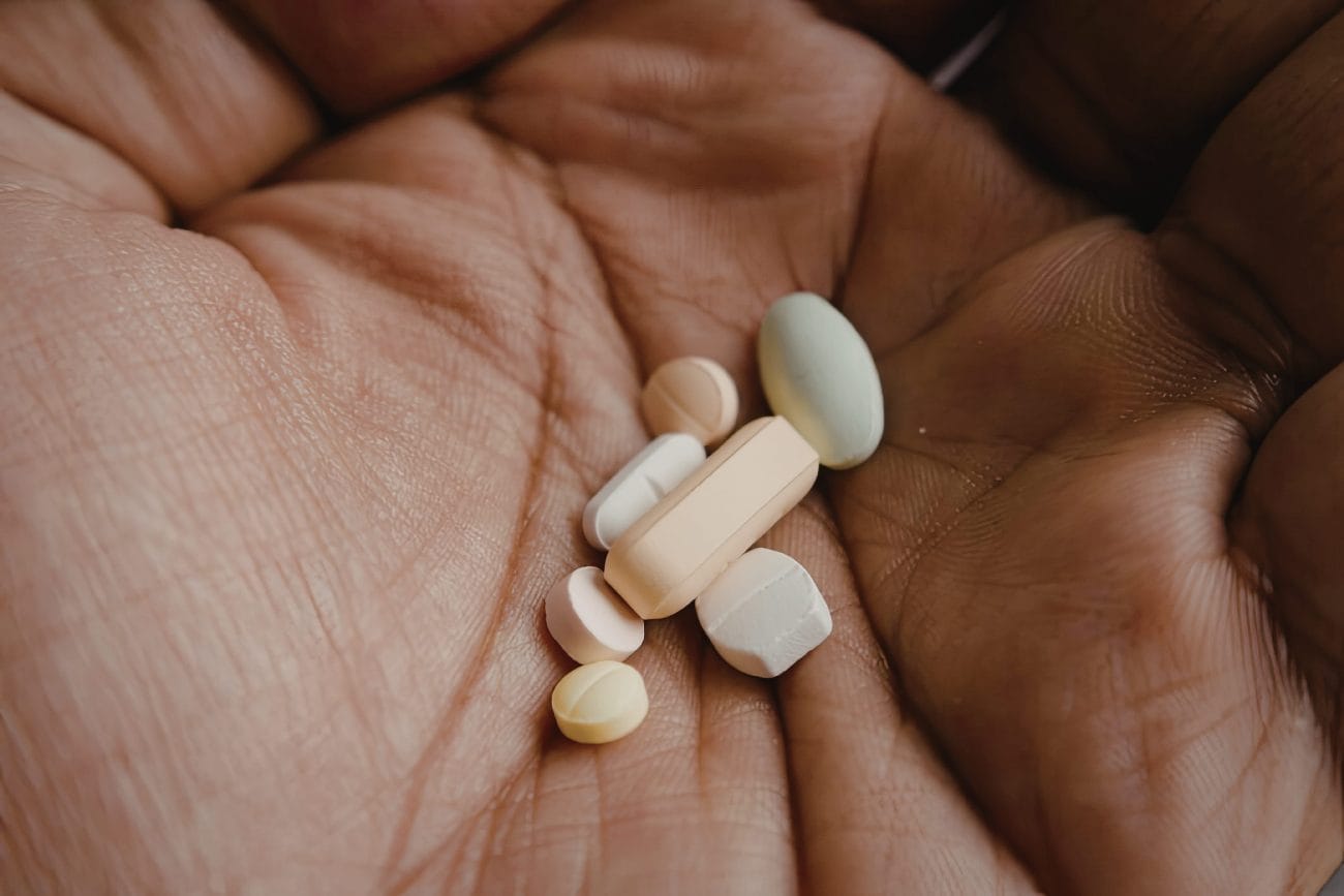 A hand holding a collection of pills in different colors and shapes - Hispamer Noticias Assorted pills held in an open cupped hand, including white tablets and a peach capsule. Hispamer Noticias