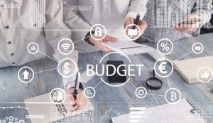 Illustration of budgeting concept with interconnected icons (currency, charts, lock, percentage) and the word BUDGET at center on a desk scene.&nbsp;Hispamer Noticias