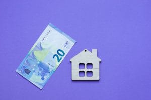 Twenty-euro banknote next to a wooden house icon on a purple background, illustrating housing costs or mortgage concepts.&nbsp;Hispamer Noticias