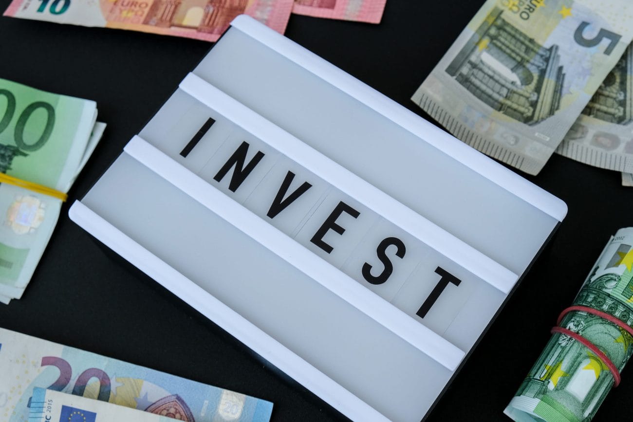 renta fija - Hispamer Noticias Close-up of euro banknotes around a white display with the word 'INVEST' in bold letters, signaling finance and investment. Hispamer Noticias