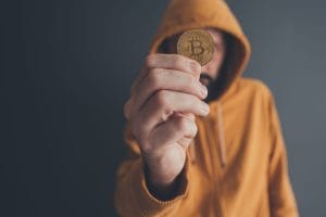 Man offering bitcoin conceptual image for payment with cryptocurrency - Hispamer Noticias Person in an orange hoodie holds a gold Bitcoin coin up to the camera, obscuring their face Hispamer Noticias