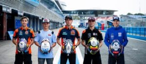 Five young race car drivers stand in the pit lane, each holding a racing helmet and wearing team uniforms, looking at the camera in a row.&nbsp;Hispamer Noticias