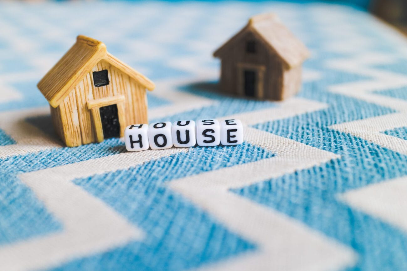 Miniature house model with - Hispamer Noticias Two wooden toy houses on a blue patterned surface with letter blocks spelling HOUSE in front. Hispamer Noticias