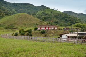 Rural hillside landscape with green rolling hills, a white building with red doors, and a wooden fence in the foreground.&nbsp;Hispamer Noticias