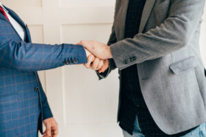 Two people in business attire shake hands, one wearing a blue check suit and the other a gray blazer.&nbsp;Hispamer Noticias