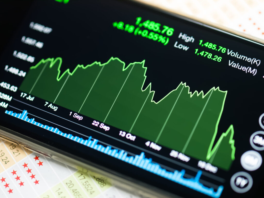 Close-up of a stock market chart on a smartphone screen with a green area graph, high/low values, and blue volume bars.&nbsp;Hispamer Noticias