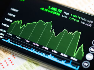 Close-up of a stock market chart on a smartphone screen with a green area graph, high/low values, and blue volume bars.&nbsp;Hispamer Noticias