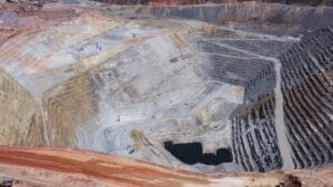 Panoramic view of the main pit of an open pit mine - Hispamer Noticias Aerial view of a large open-pit mine with stepped, terraced walls and a dark water-filled pit at the bottom center. Hispamer Noticias