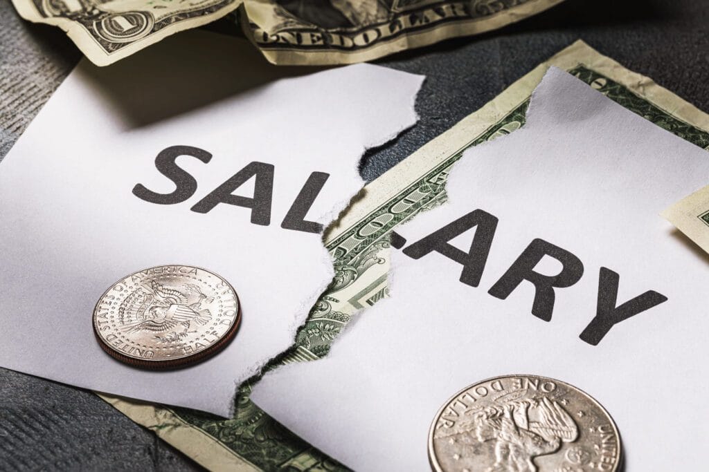 Torn salary document with dollar bills and coins scattered on a dark surface, conveying pay or wages.&nbsp;Hispamer Noticias