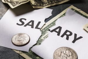 Torn salary document with dollar bills and coins scattered on a dark surface, conveying pay or wages.&nbsp;Hispamer Noticias