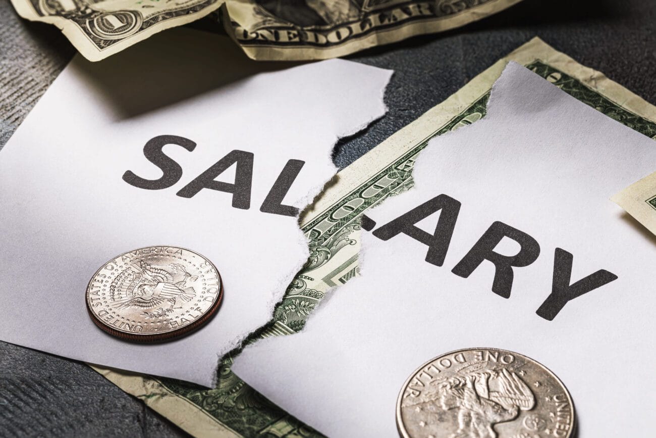 Torn salary document with dollar bills and coins scattered on a dark surface, conveying pay or wages.&nbsp;Hispamer Noticias
