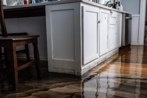 Flooded apartment due to a leak from a burst pipe or after a flood - Hispamer Noticias Kitchen with white base cabinets and a wooden chair, water pooling along the base of the cabinets on a glossy floor. Hispamer Noticias